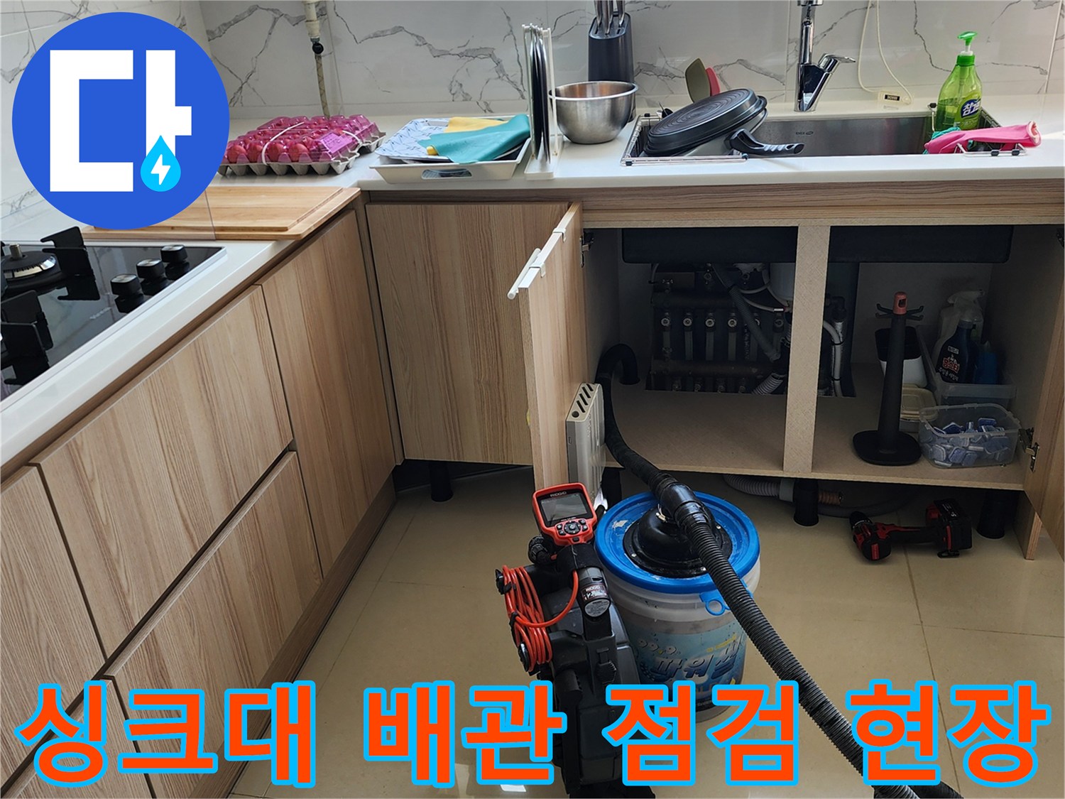 싱크대 아래쪽 누수 지점을 찾기 위해 장비를 활용하여 내부를 점검하는 사진입니다.