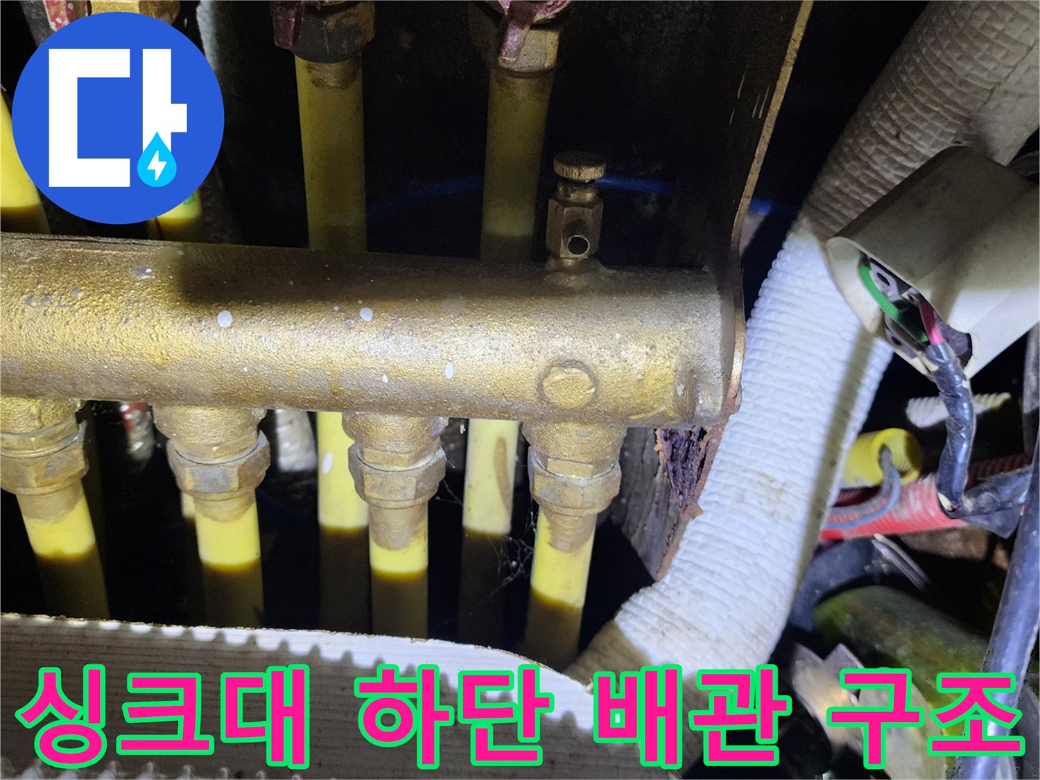 싱크대 밑바닥에 노출된 다수의 수도 배관과 밸브 연결 부위입니다.