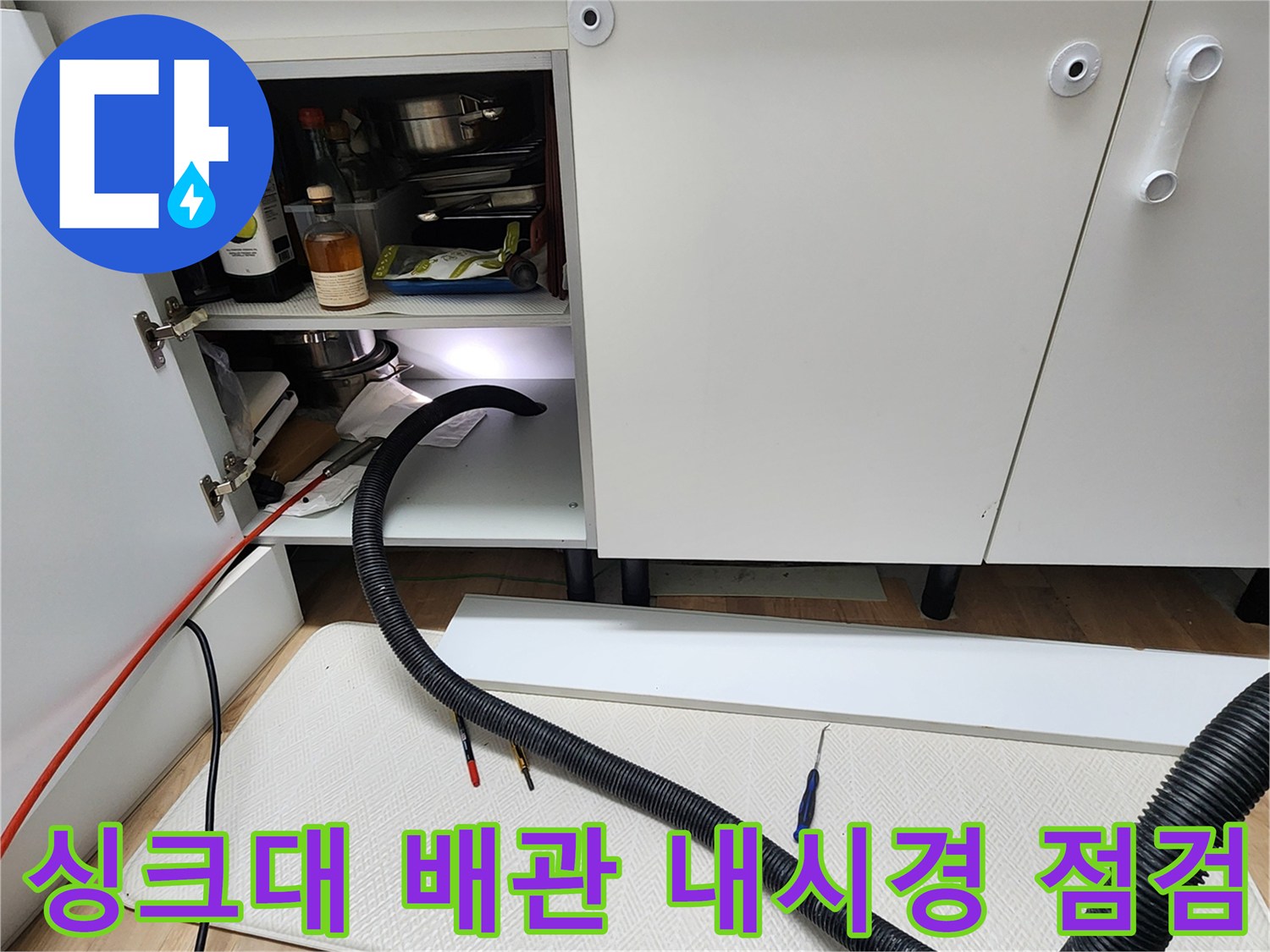 싱크대 밑 어두운 공간에 설치된 내시경 카메라와 연결된 검은색 호스의 모습입니다.