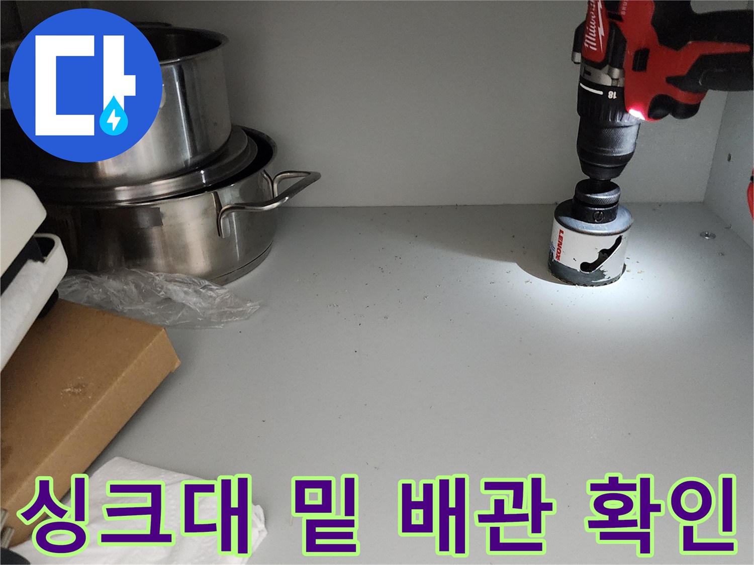 싱크대 하부장 내부의 밝은 조명과 드릴 장비가 보이는 작업 현장