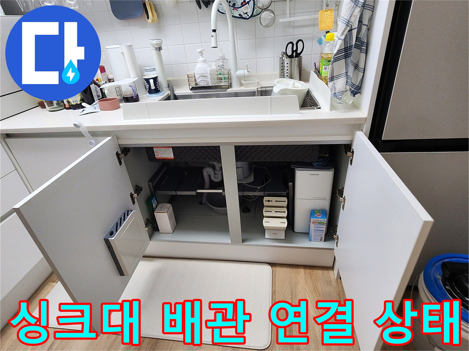 주방 싱크대 하부장 문을 열고 내부 배관 시설물을 점검하는 모습