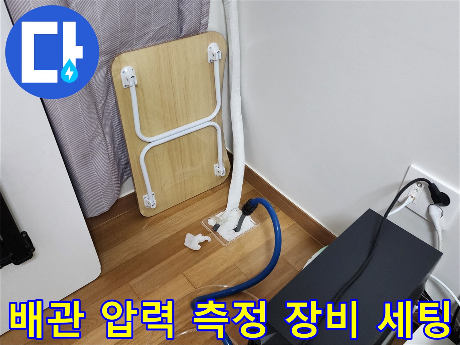 바닥 배관 연결부에 연결된 파란색 호스와 테스트용 장비 모습입니다.