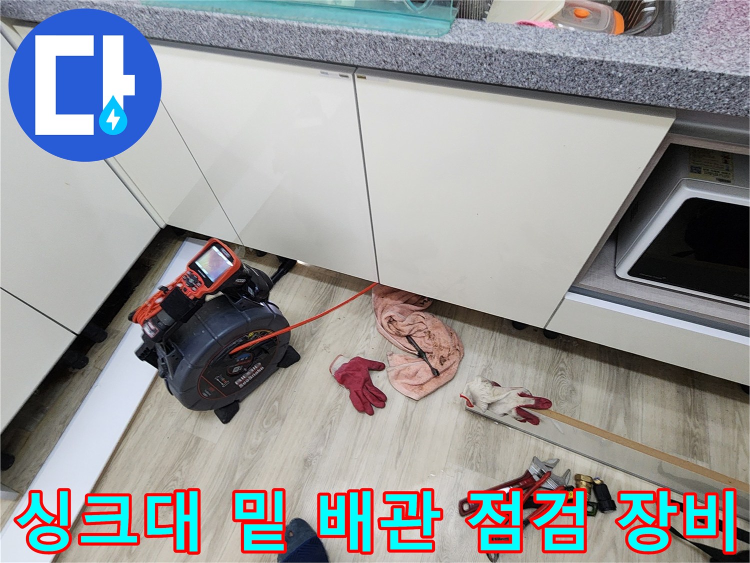 싱크대 아래 공간에 놓인 디지털 압력계와 각종 수공구 및 장갑