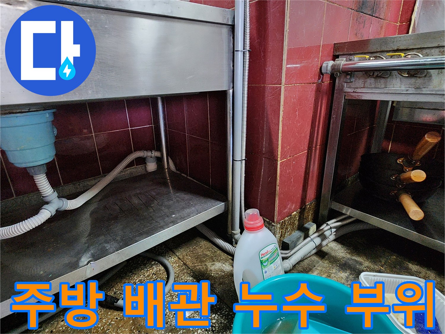 싱크대 하부장 아래쪽 배수 호스와 젖은 바닥 타일 모습