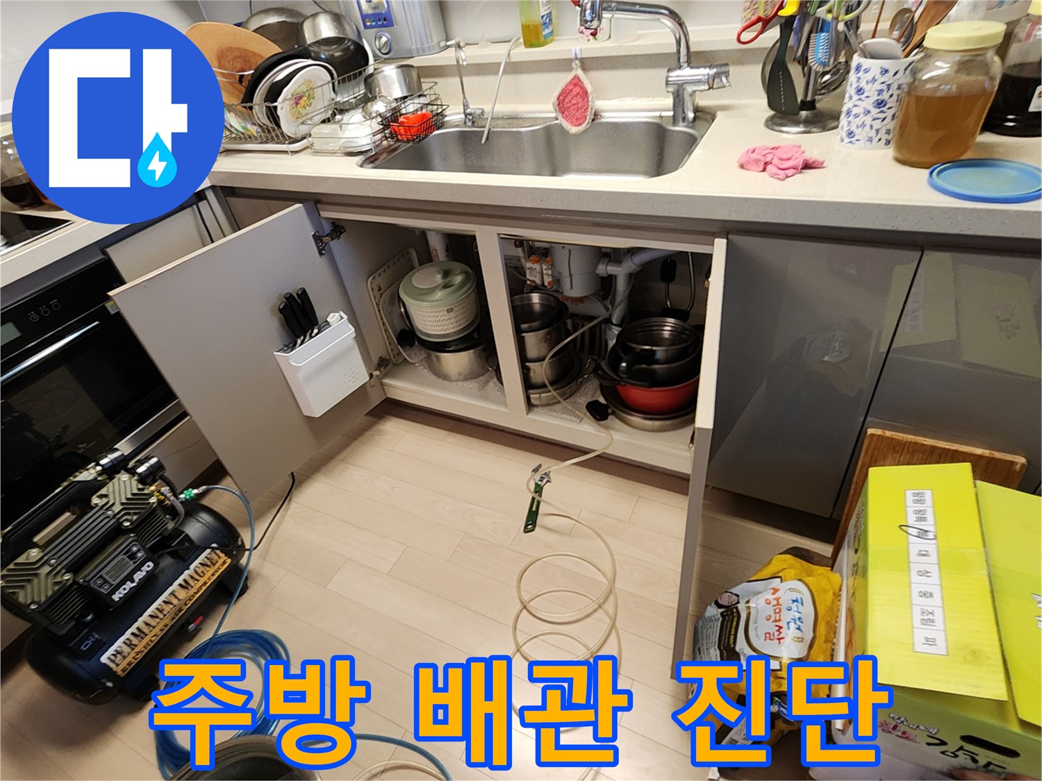 싱크대 하부장 내 배수 호스와 콤프레셔 장비 배치