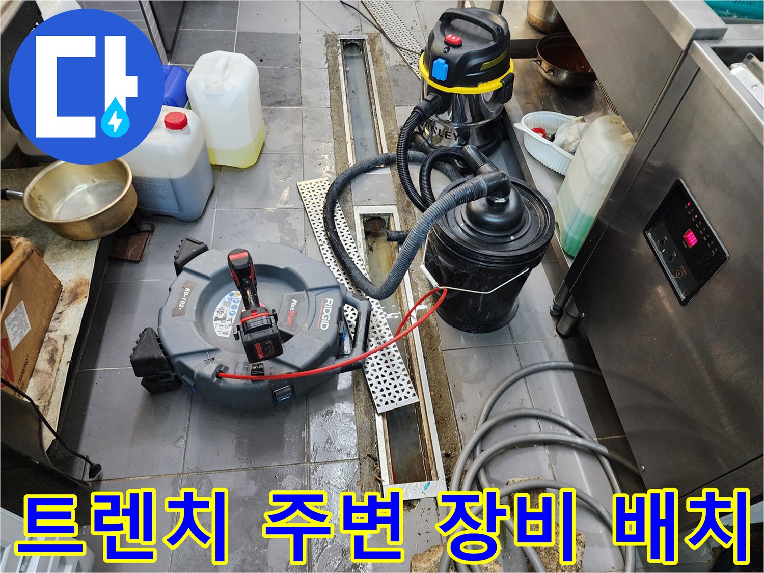 주방 바닥 배수 트렌치 옆에 놓인 배관 청소용 전문 기기들