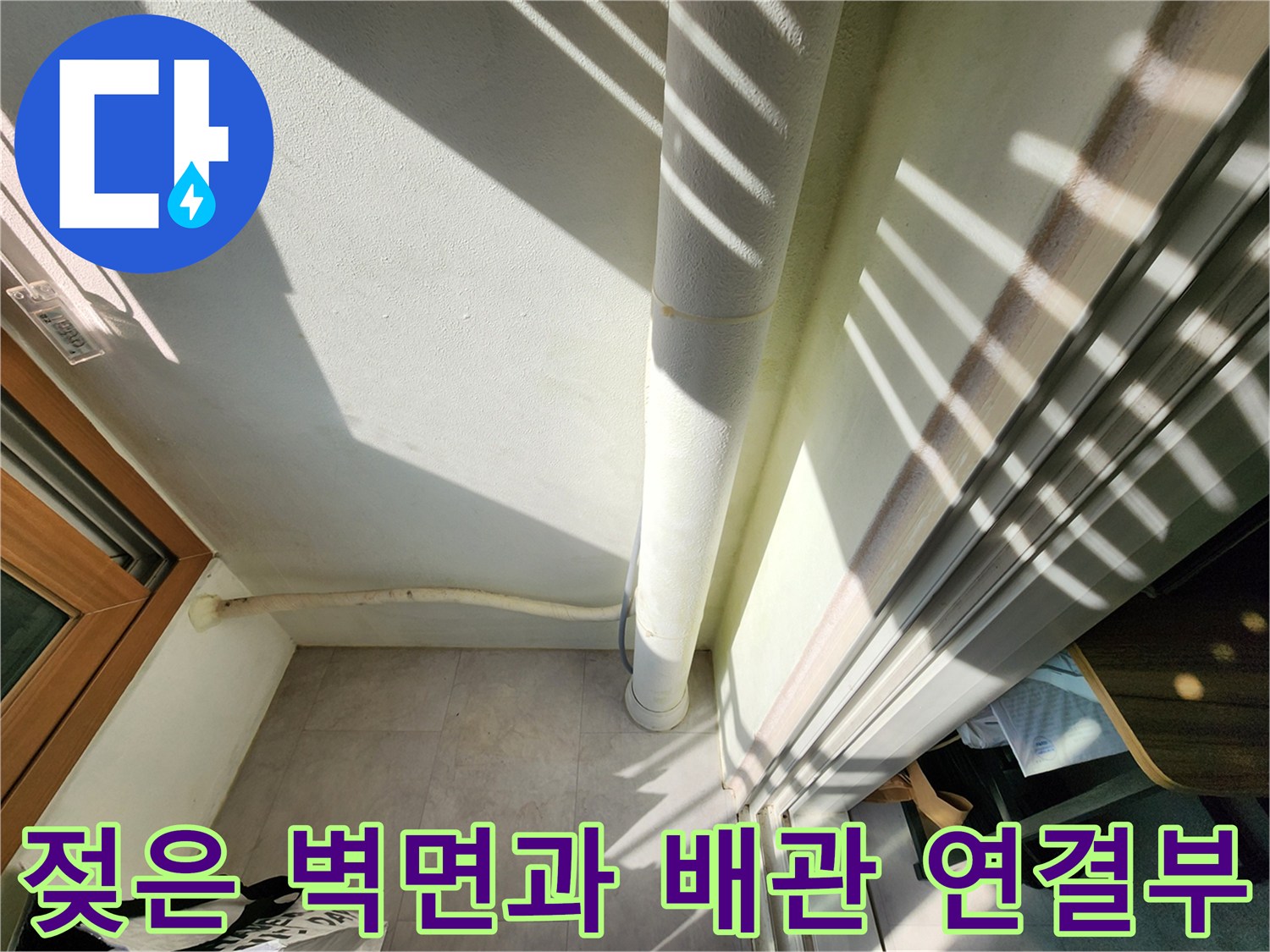 흰색 수직 배관 하단의 습기 젖은 벽면 모습