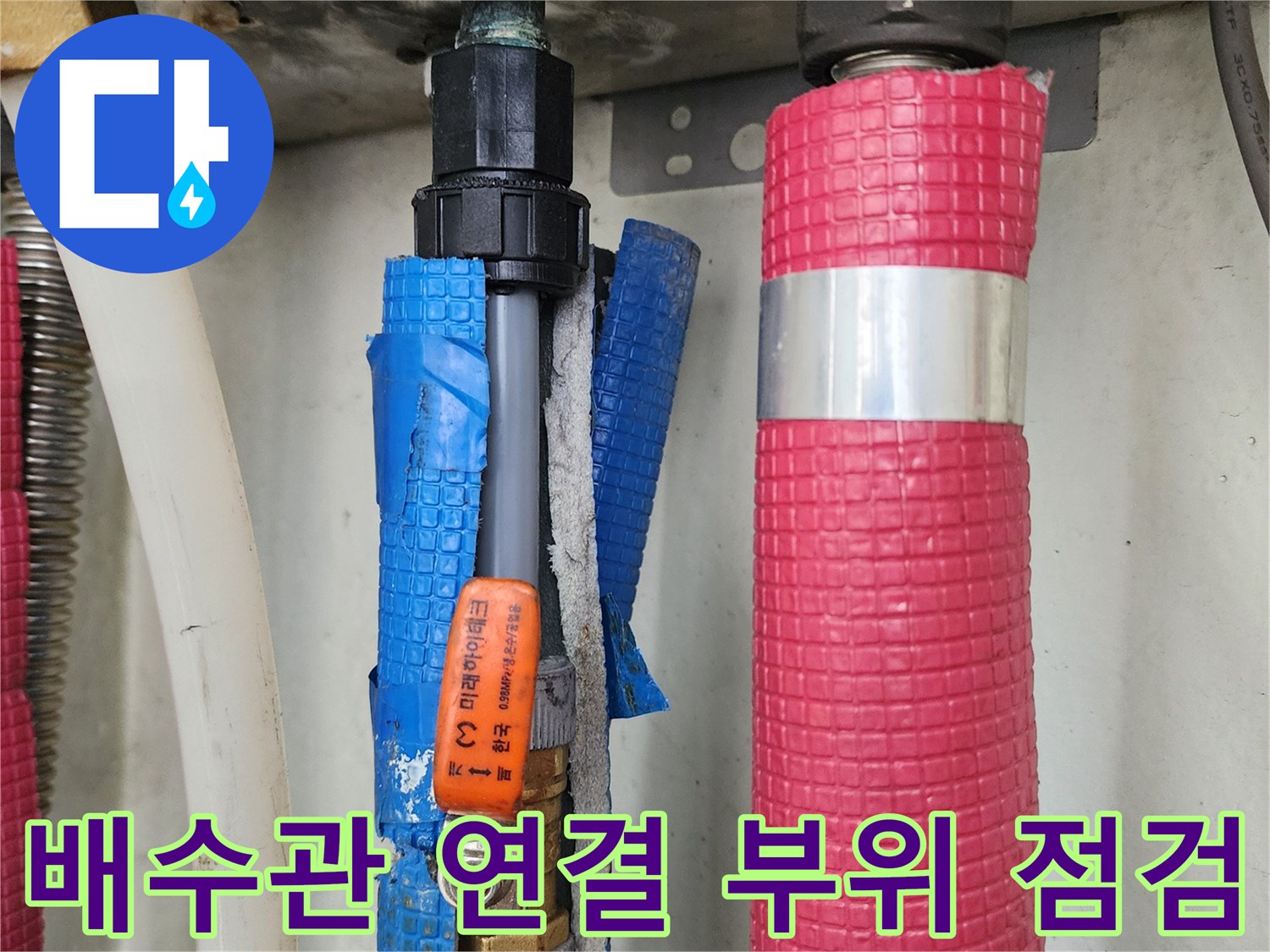 주방 배관의 붉은색 보온재와 파란색 마감재가 보이는 하부 배관 상세 사진