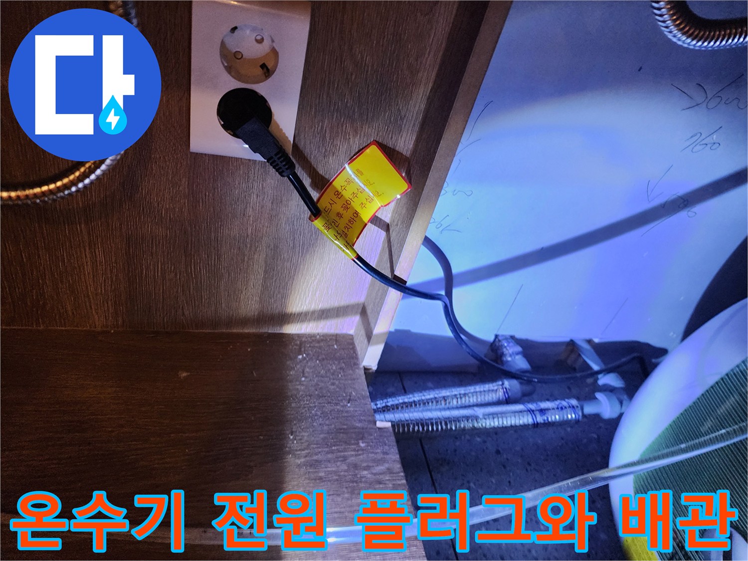주방 하부장 내부의 전기 콘센트 및 금속 재질의 온수기 배관