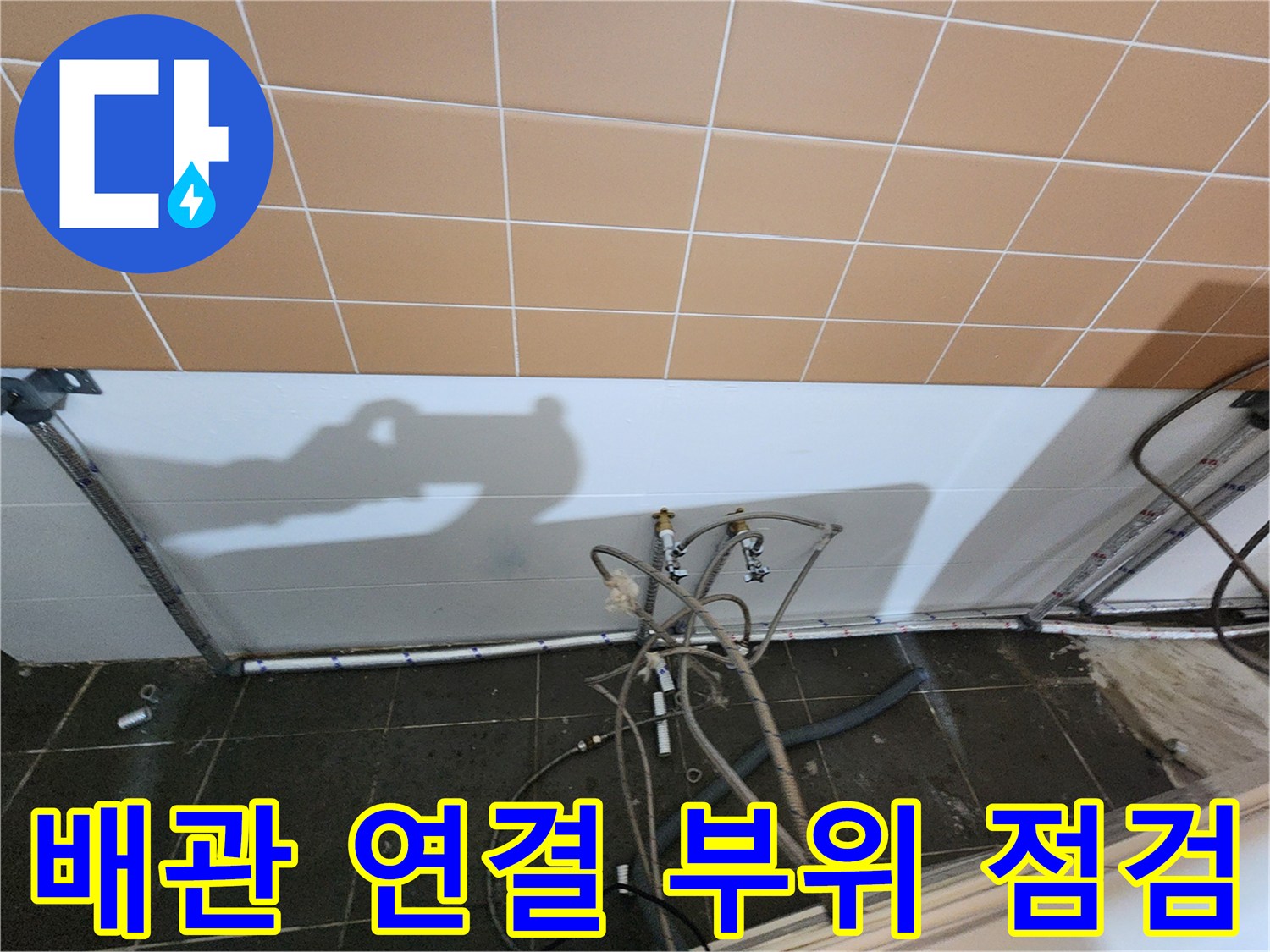 벽면 타일 아래쪽 샴푸대 배관들의 결합 상태를 촬영한 사진