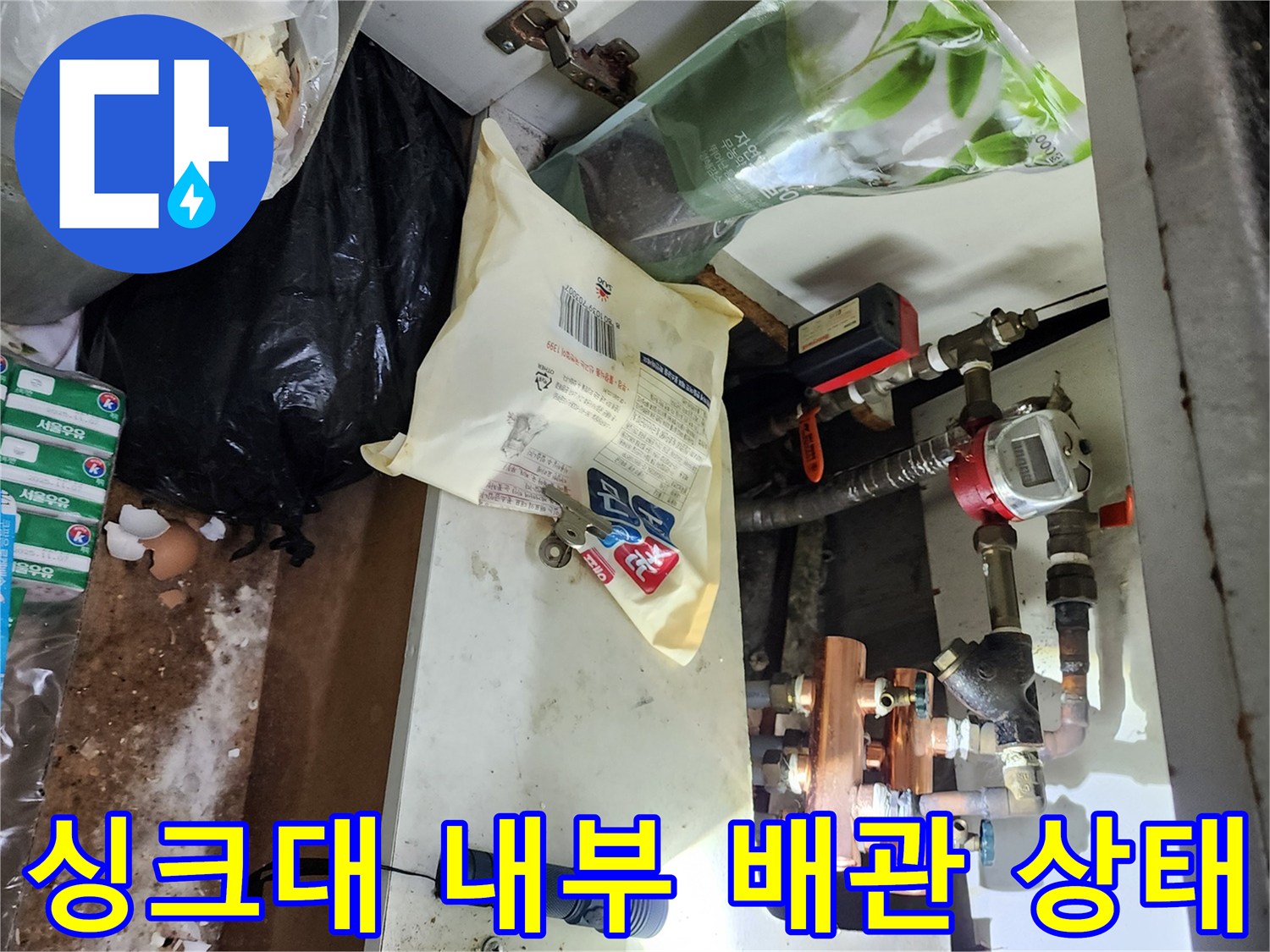 손전등 빛으로 비춘 싱크대 하부의 금속 및 플라스틱 배관
