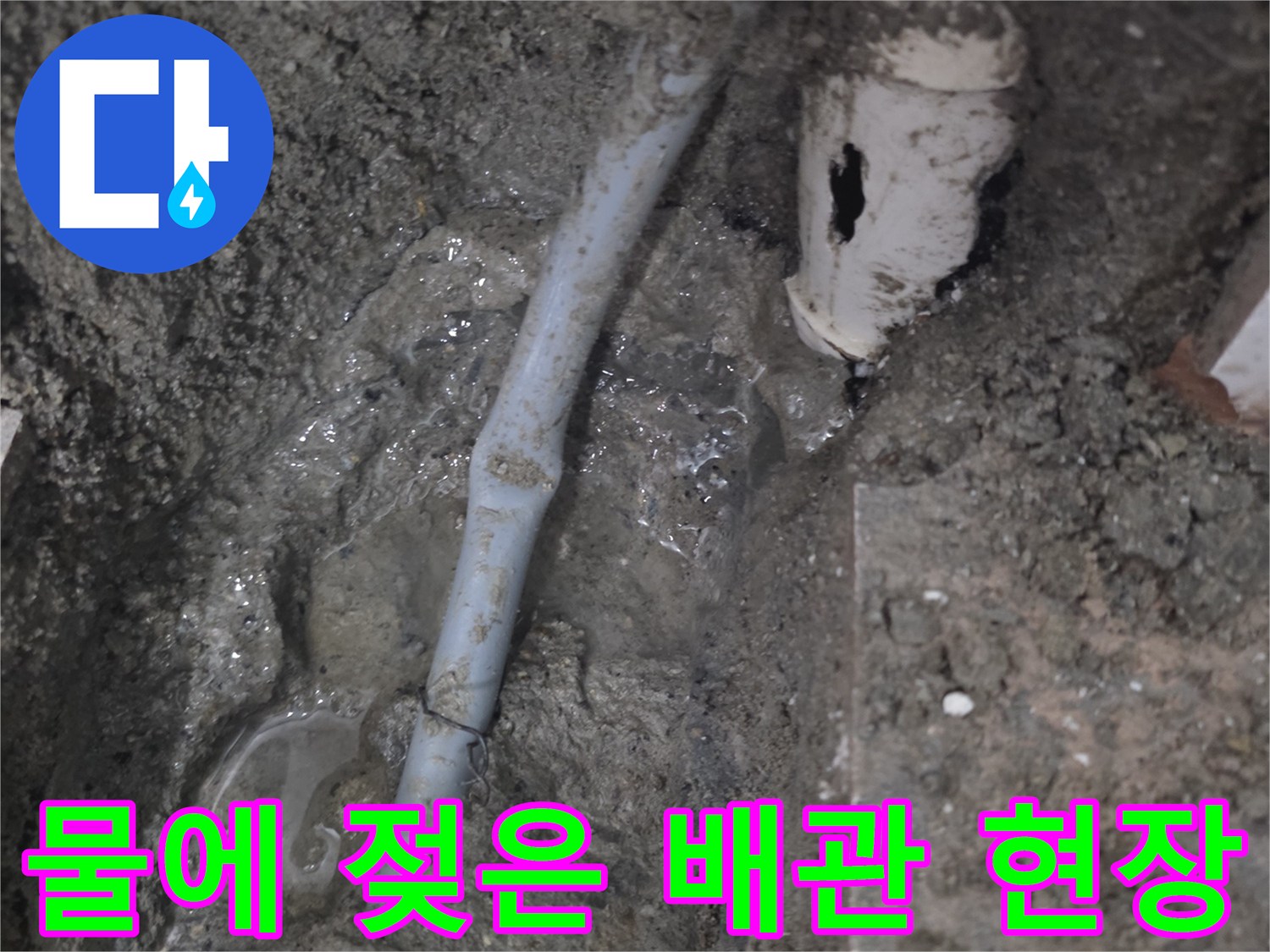 물기가 흥건한 흙과 노출된 백색 수도 배관의 모습