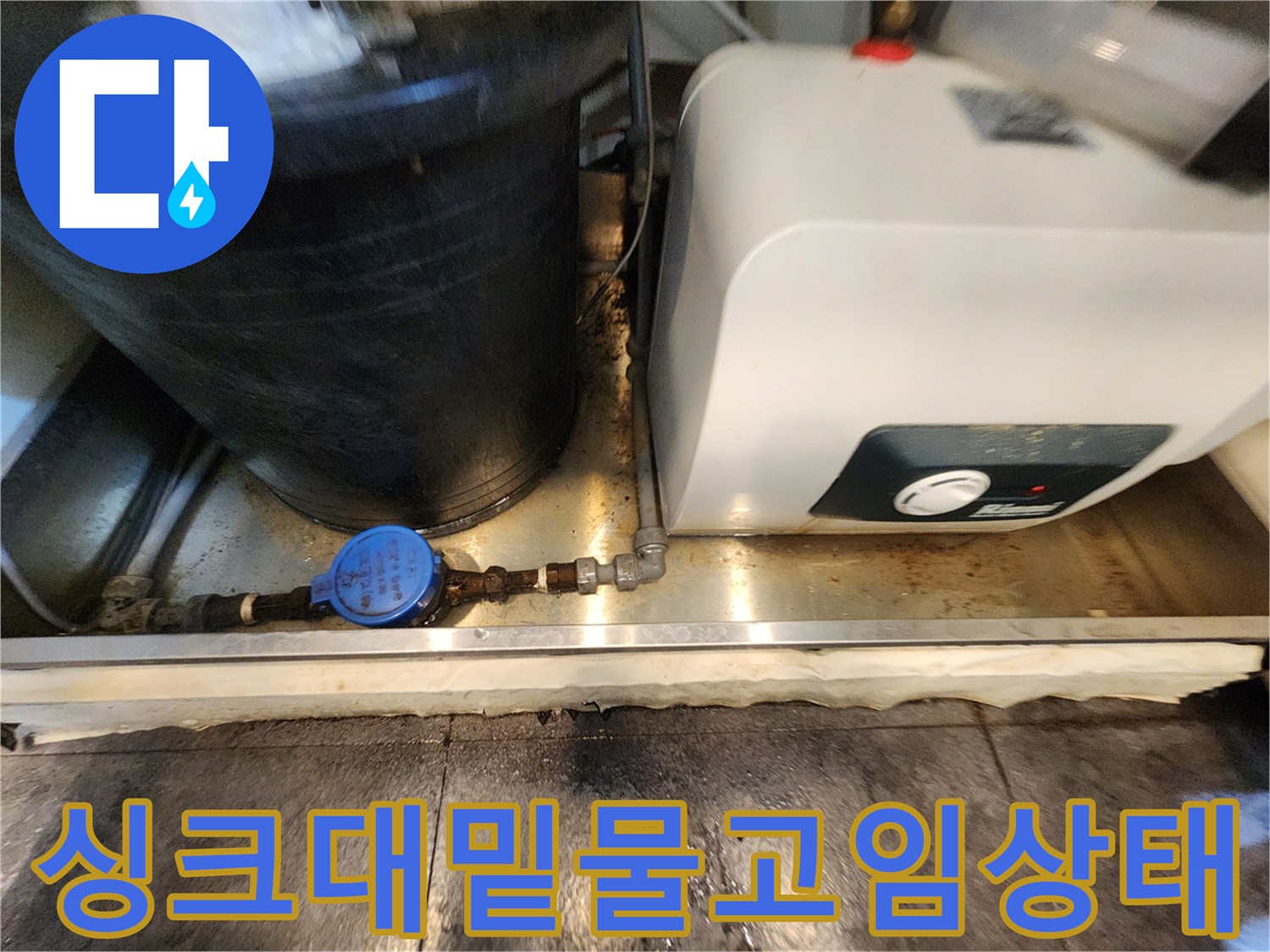 싱크대 하단부의 젖은 바닥과 복잡한 배관 설비 사진