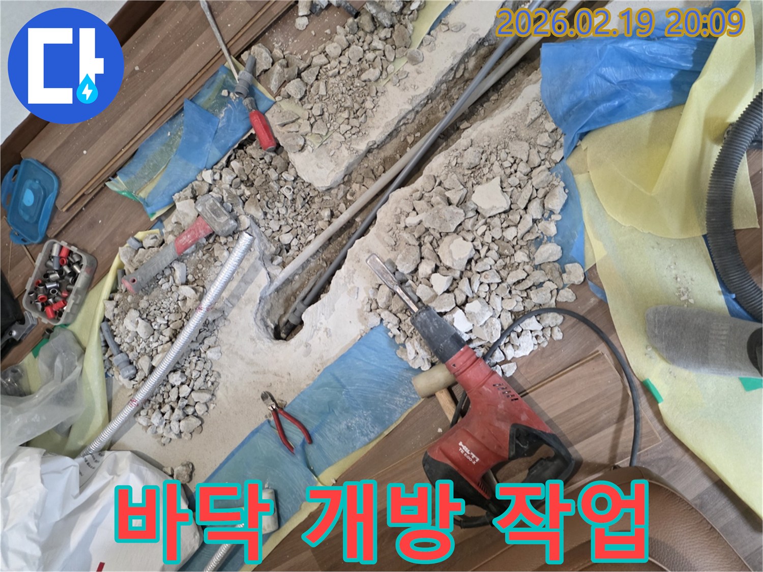 누수-공사-현장에서-바닥이-파쇄되고-배관이-노출된-모습-드릴과-망치-등-공구들이-놓여있습니다.