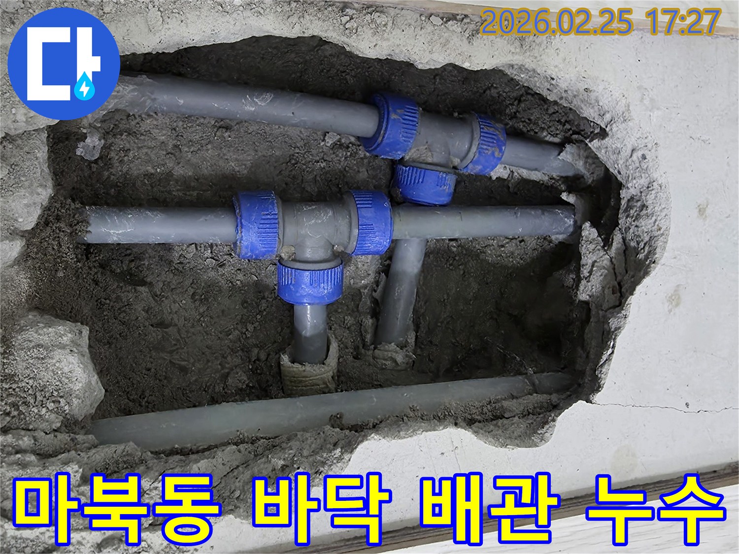 콘크리트 바닥 아래에 파묻힌 회색 배관과 파란색 연결 부속들이 보이는-누수 수리 현장