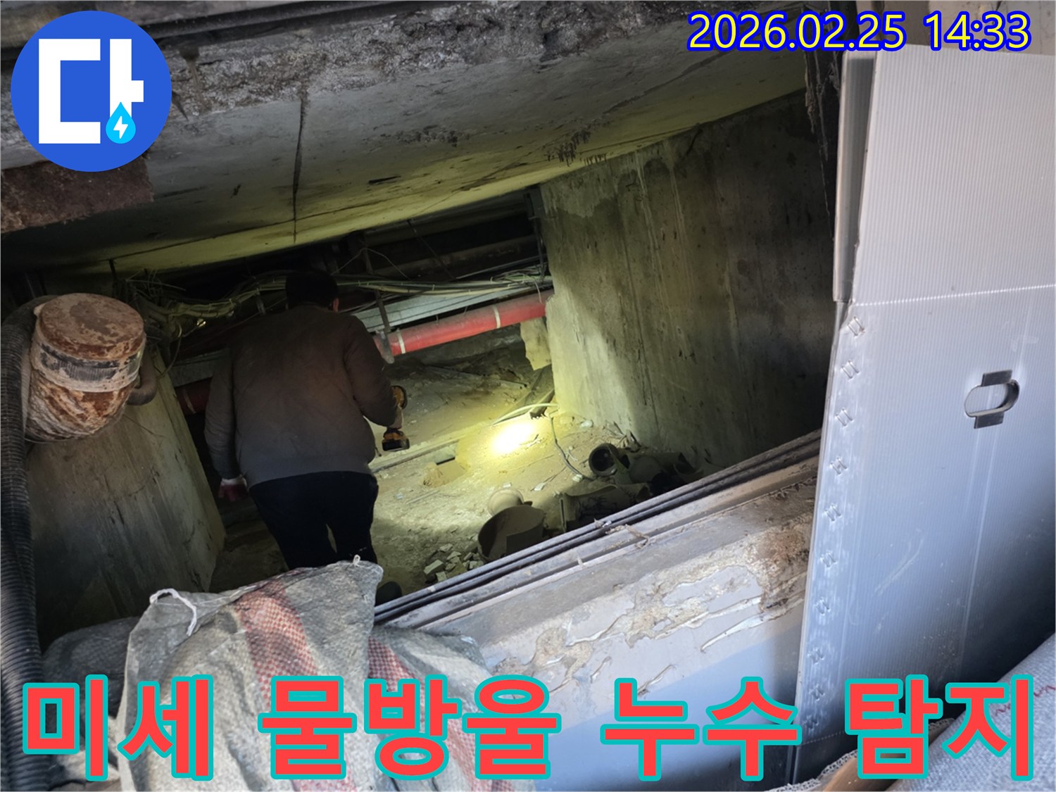 누수 전문 엔지니어가-어둡고 좁은 공간에서-손전등을 비춰가며-배관의 미세한 물방울까지-놓치지 않고 탐지하는 모습입니다.