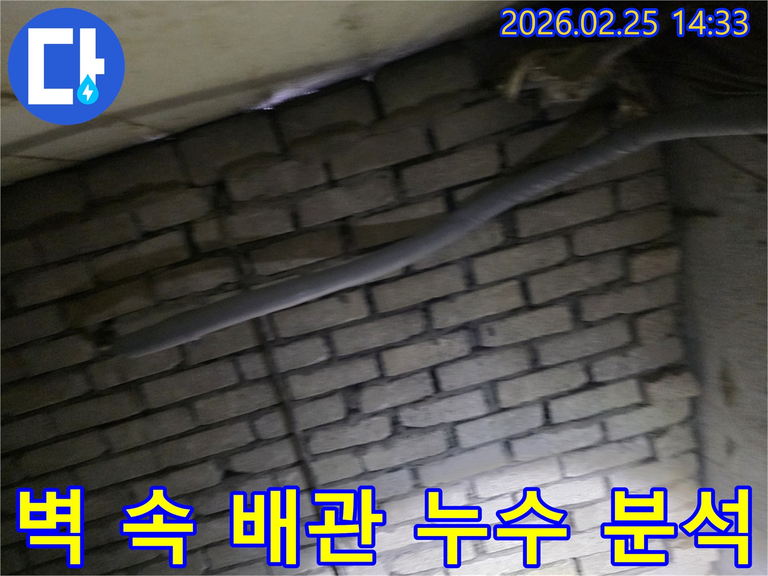 어두운 벽돌 벽면을 배경으로-단열재로 감싸인 배관과-다른 배선이 누수 여부를-확인하기 위해 촬영된 현장 이미지입니다.