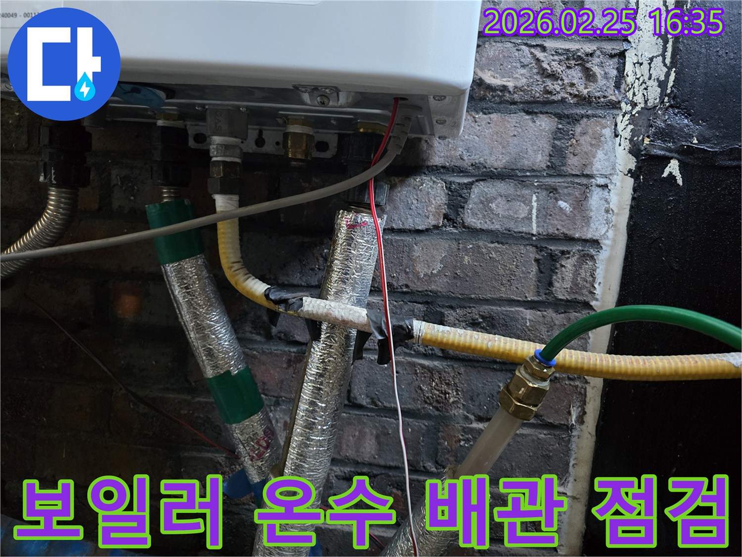 이 이미지는-벽에 설치된-보일러 하단부의-온수 배관과-난방 배관-그리고-전선이-연결된-모습을-보여주며-온수 누수 여부를-확인하기 위한-정밀한 점검이-진행되고-있음을-암시합니다.