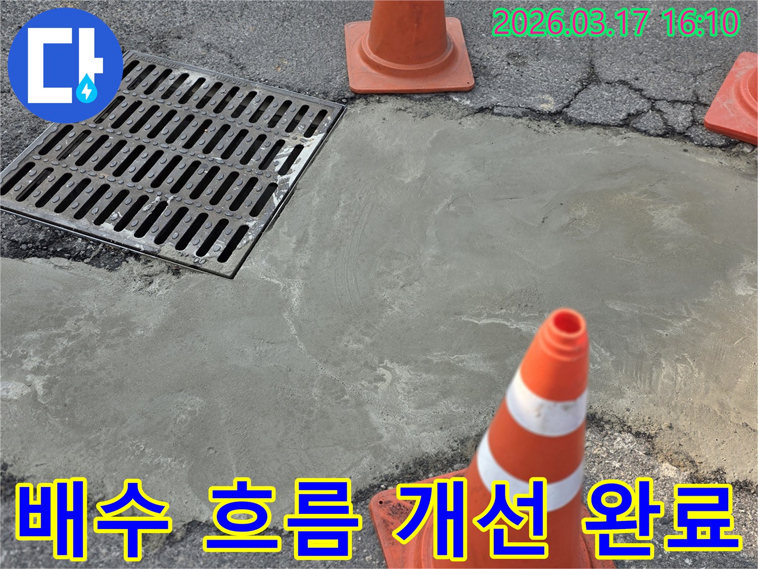 이 이미지는 양주시 율정로의 외부 바닥 누수 문제로 인한 배수 흐름 개선 작업이 완료된 상태를 보여주며-새로운 시멘트 마감과 안전 콘이 놓여 있습니다.