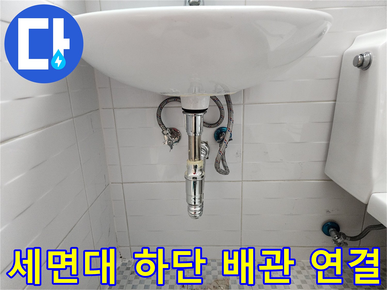 세면대 아래 벽 타일에 설치된 은색 수도 부속
