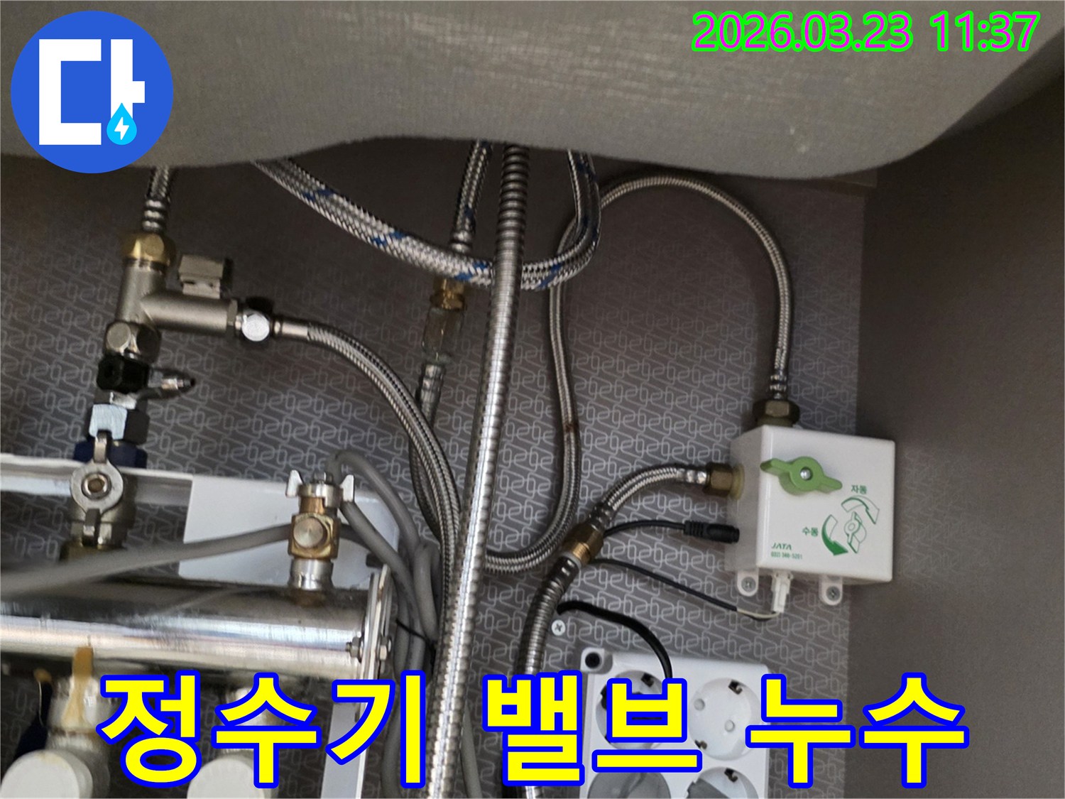 주방 싱크대 아래에 설치된 정수기 연결-밸브와 수도-호스-배관-전기 콘센트가 보이는 현장 사진입니다.
