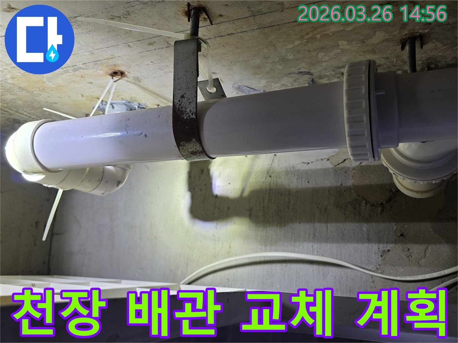 콘크리트 천장에 고정된-오래된 하얀색 배관과-녹슨 지지대의 모습으로-천장 배관 교체 공사 계획 현장을 보여줍니다
