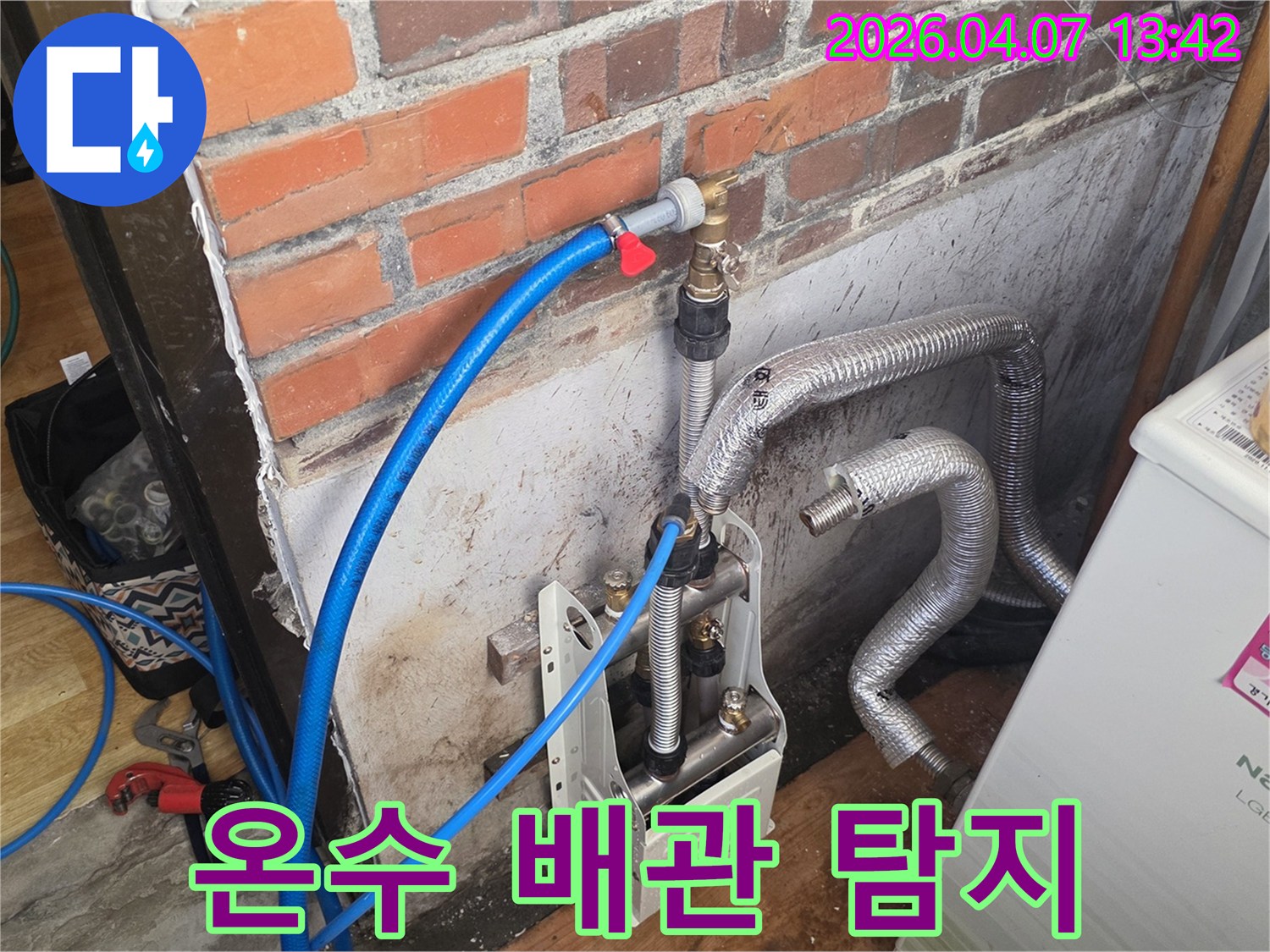 벽돌 벽 옆에-온수 배관과-연결된 누수 탐지 장비가-설치되어 있으며-정확한 누수 지점을 찾기 위한-준비가 진행 중입니다.