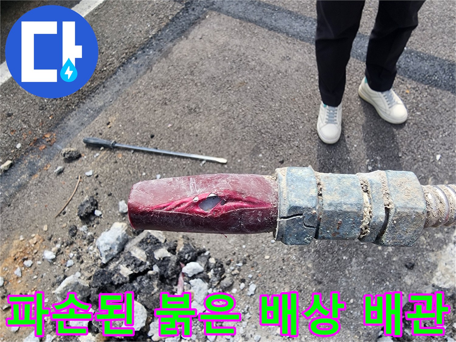 아스팔트 하단에 노출된 파손된 붉은색 급수 배관