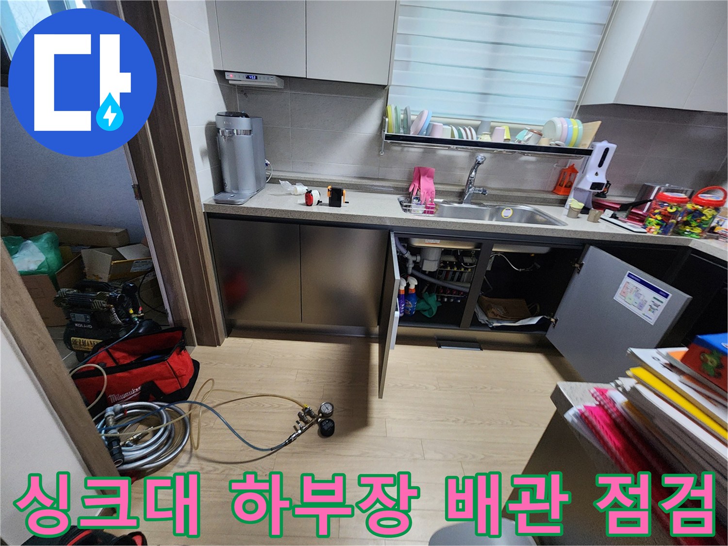 주방 싱크대 아래쪽-열려있는 하부장 내부의 복잡한 배관과 탐지 장비들