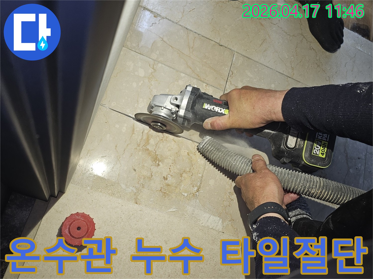 온수관 누수 해결을 위해 작업자가 그라인더로 바닥 타일을 절단하고-있으며-동시에-흡진기로-먼지를-제거하여-깨끗한-작업-환경을-유지하는-모습입니다.