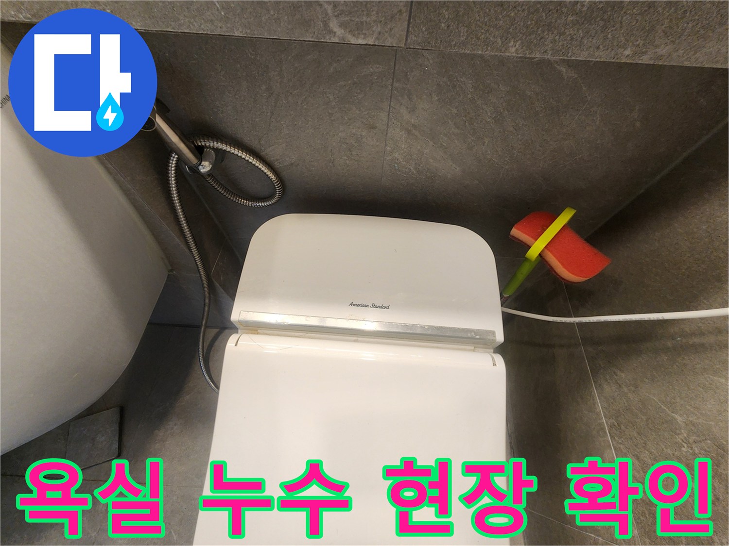 어두운 타일 벽면과-하얀 변기-그리고 청소 도구가 놓인 욕실 전경입니다.