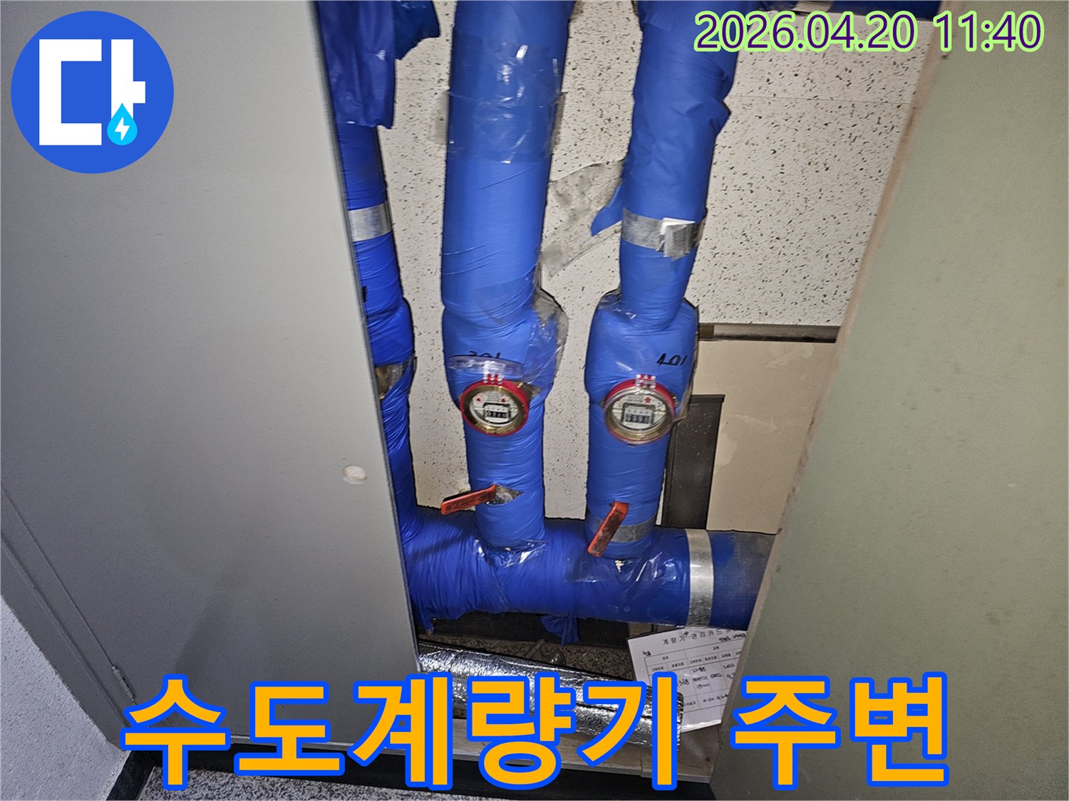 파란색 단열재로-감싸진-수도관과-두 개의-수도계량기가-보이는-누수-점검-현장-사진입니다.