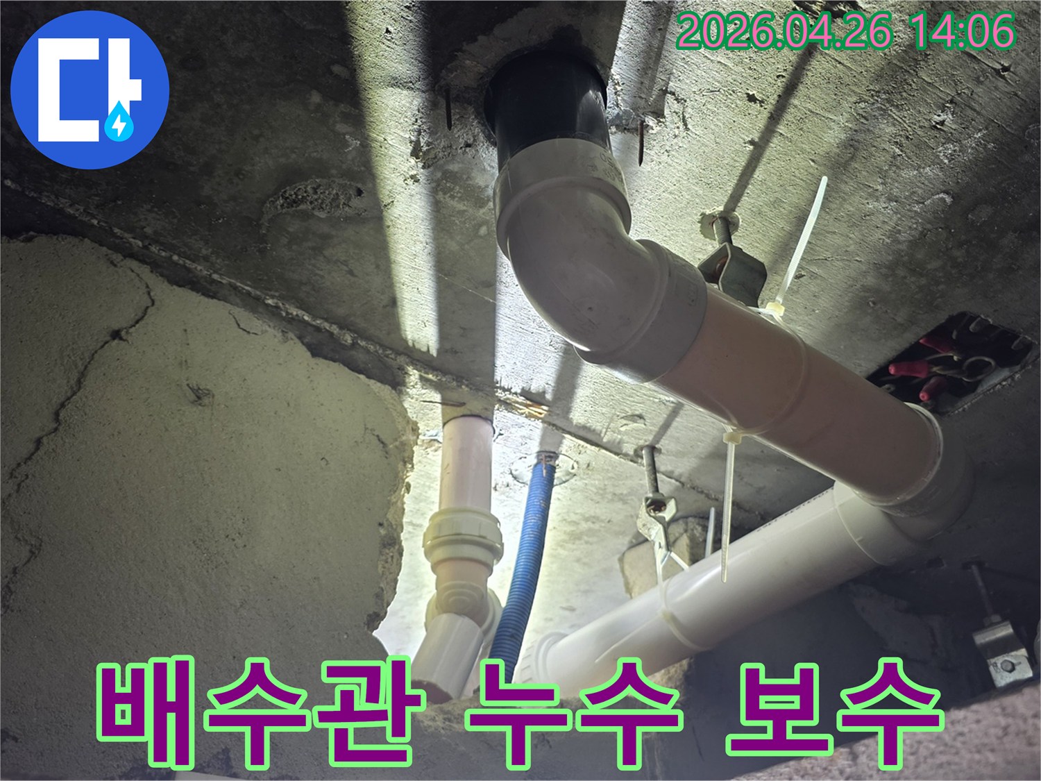 이 이미지는 아파트 천장 아래의-오래된 배수관에서 발생한-누수 문제를 해결하기 위해-보수 작업을 진행하는-전문가의 모습을 담고 있습니다.