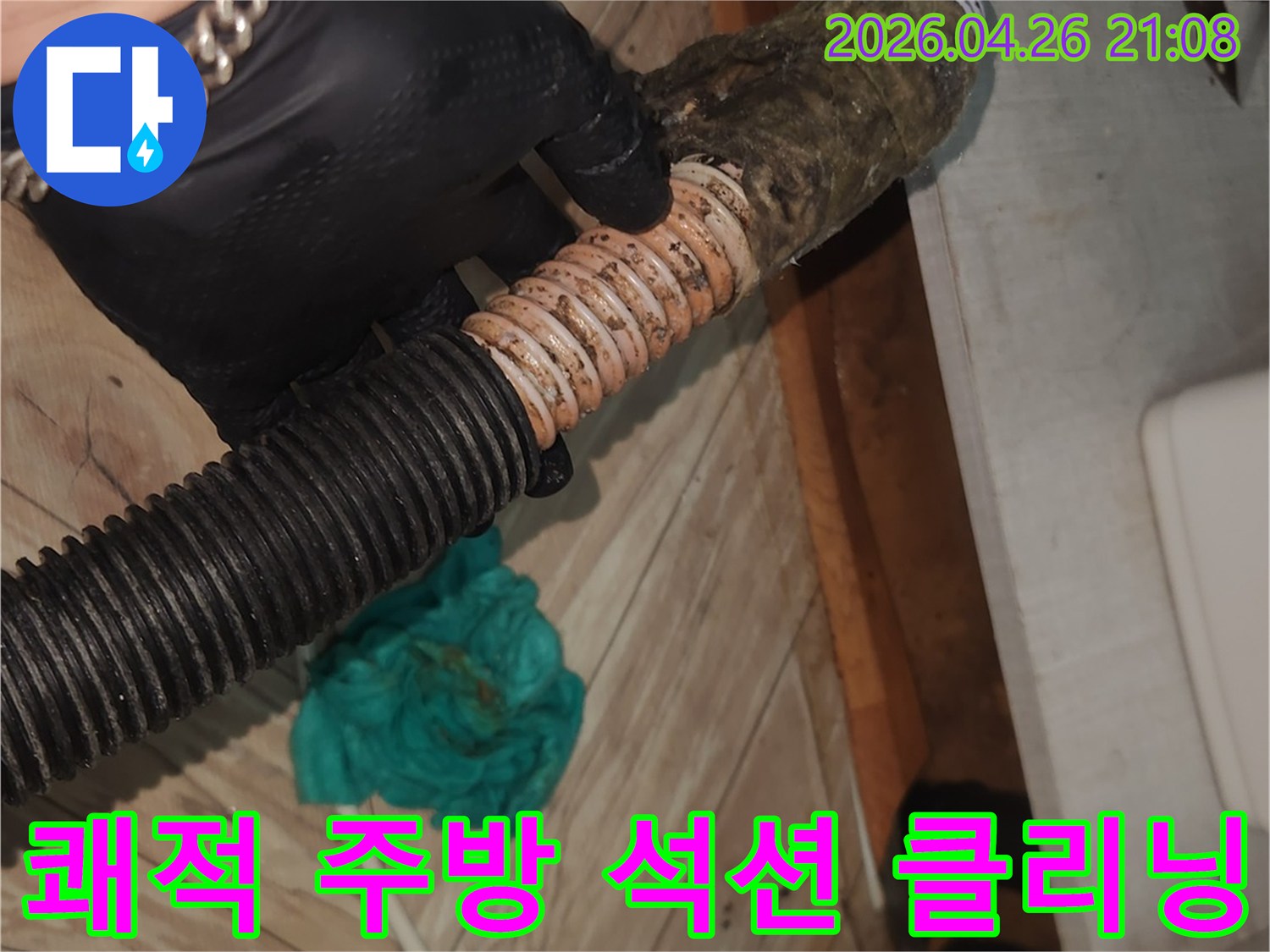 검은색 장갑을 낀 작업자가-오염된 싱크대 배수 호스를-석션 장비로 깨끗하게 청소하여-쾌적한 주방 환경을 만드는 중