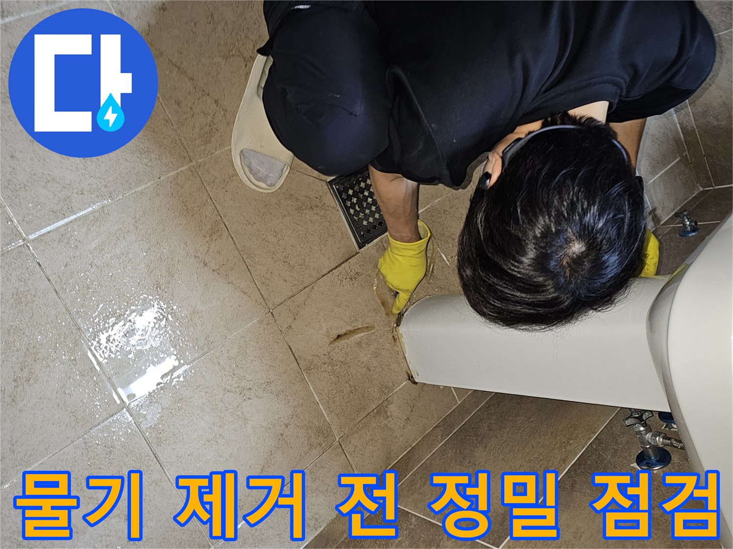 전문 엔지니어가-노란 장갑을 끼고-욕실 바닥의 젖은 타일과-세면대 하단부를-집중적으로 관찰하며-누수 지점을 파악하고 있습니다