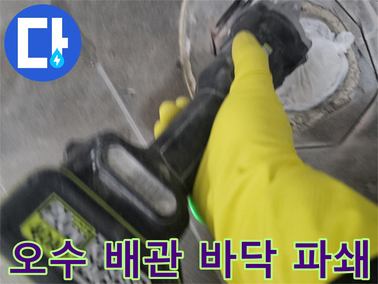 노란색 안전 장갑을 착용한 기술자가-전동 절단기로-오수 배관 주변의 바닥 타일을-신중하게 잘라내어-파쇄하는 모습입니다.