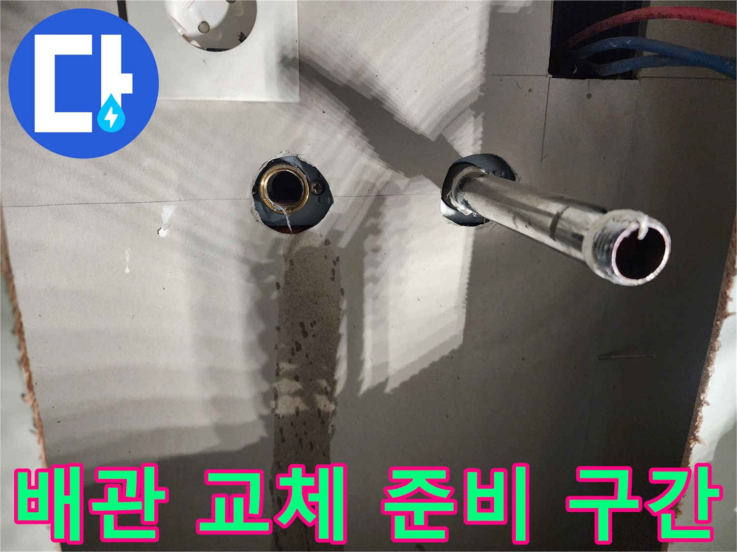 타공된 벽면 사이로 보이는 금속 배관과 파란색 유연 관재