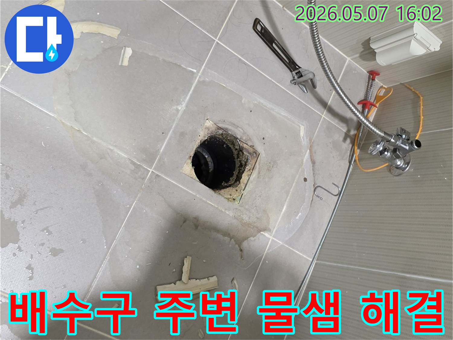 욕실 바닥의 배수구 주변에 물기가 보이고 타일이 제거된 모습-물샘 현상을 해결하기 위한 보수 작업 현장입니다