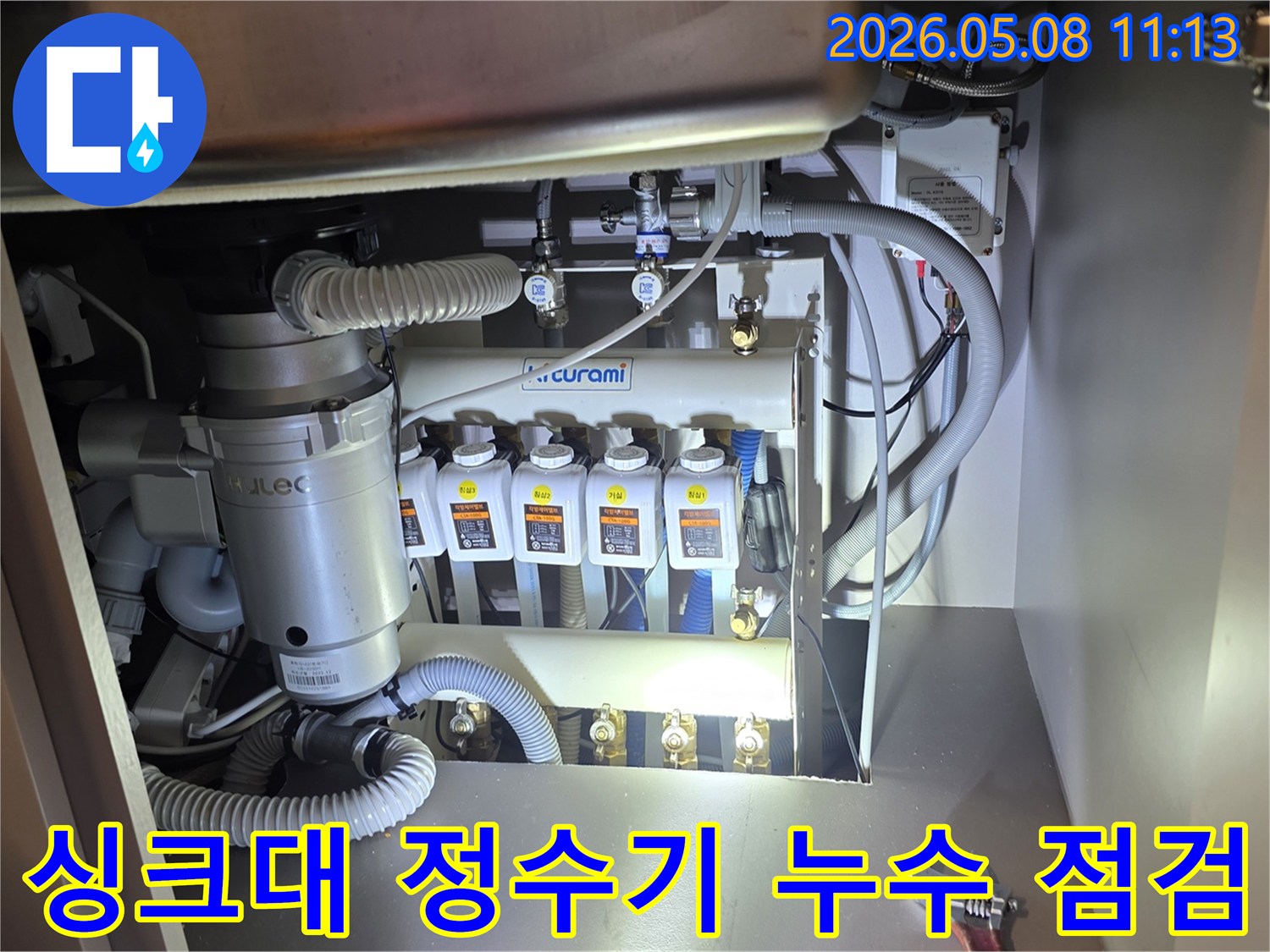 이 이미지는 싱크대 하부-정수기 배관과 음식물처리기-주변에서 발생한 누수를-전문가가 정밀하게 점검하는-현장을 보여줍니다
