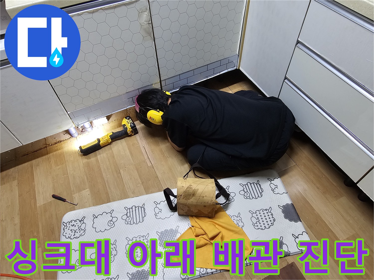 싱크대 밑 공간의 배관 연결 부위를 정밀하게 조사하는 작업 모습
