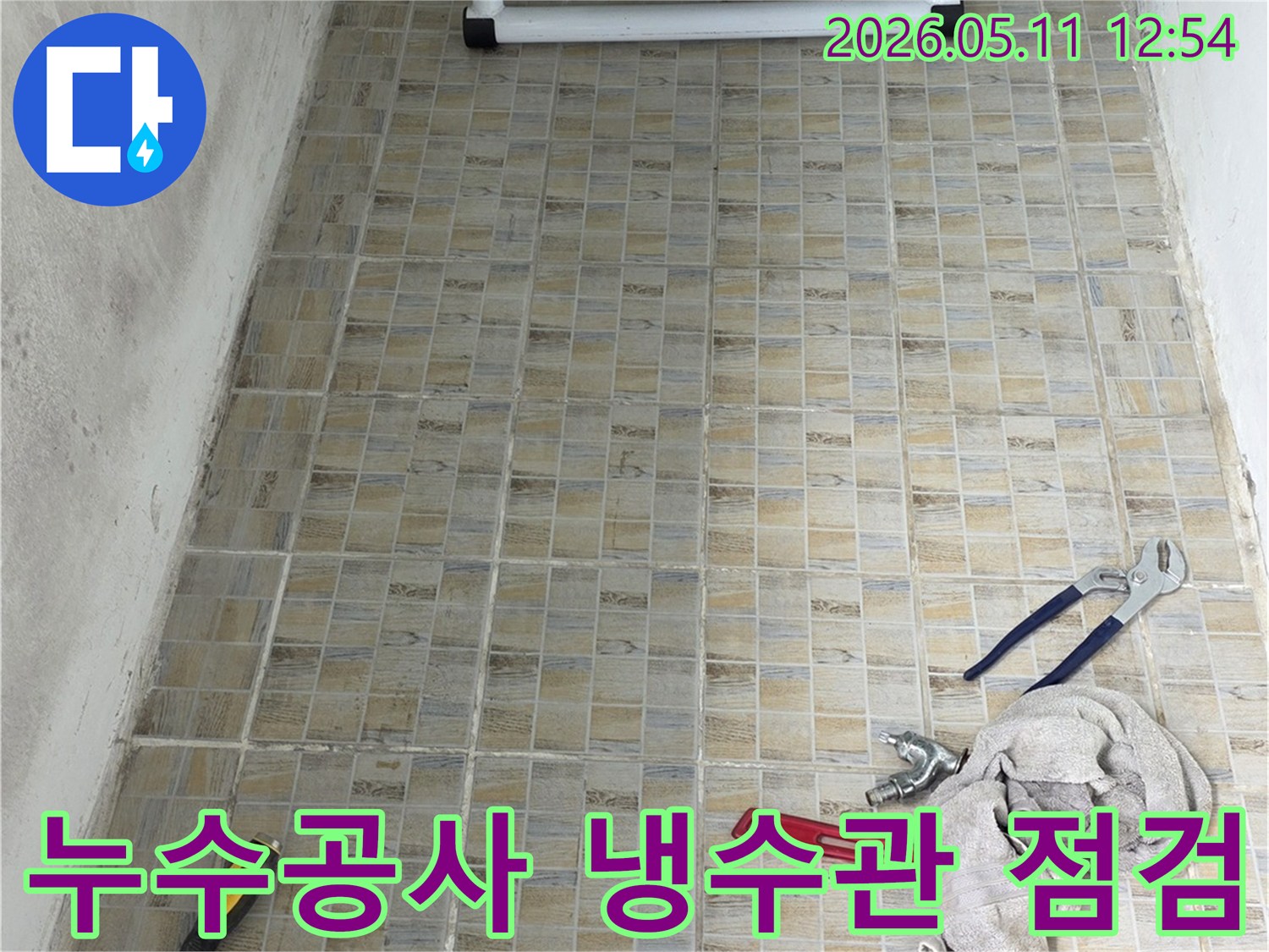 누수 공사 현장에서-타일 벽면과-냉수관 점검에 필요한 공구들이 놓여있는 모습
