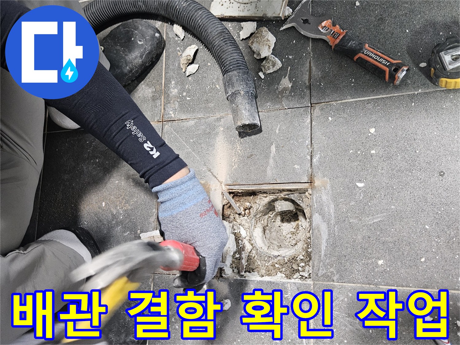 망치와 정을 사용하여 하수구 주변의 타일을 깨뜨리는 공사 현장입니다.