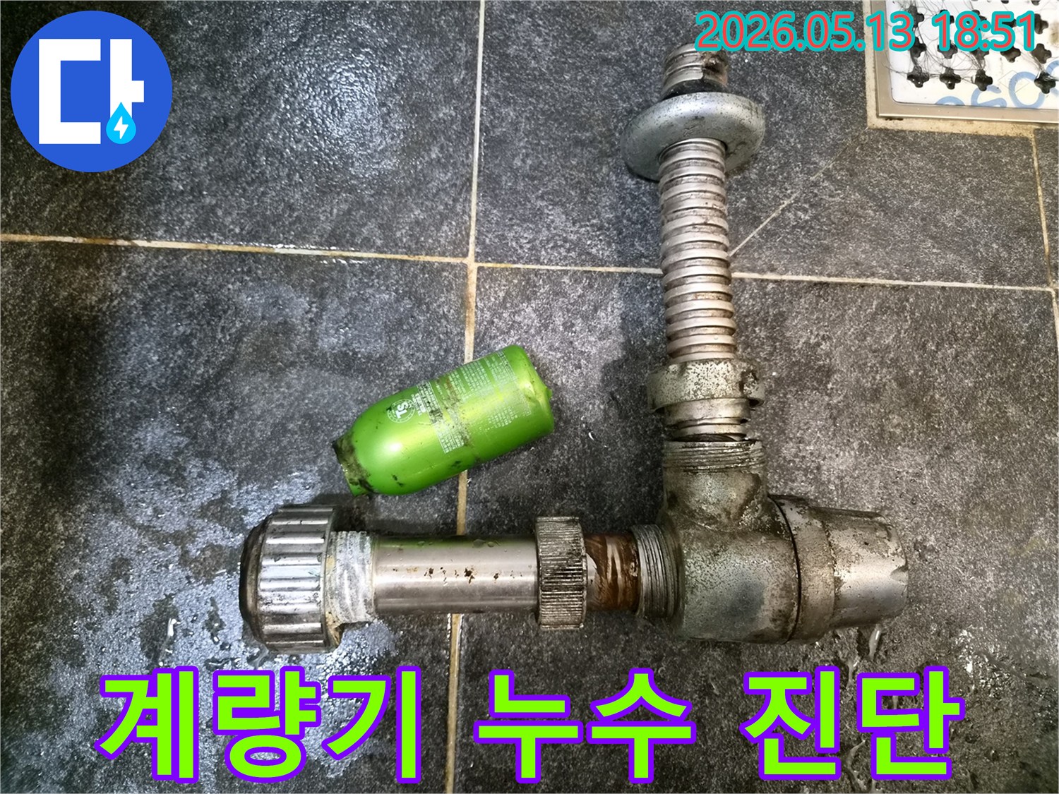 어두운 타일 바닥 위에-녹슨 배관 부품과-초록색 샴푸통이 놓여있는-수도 계량기 누수 진단 현장