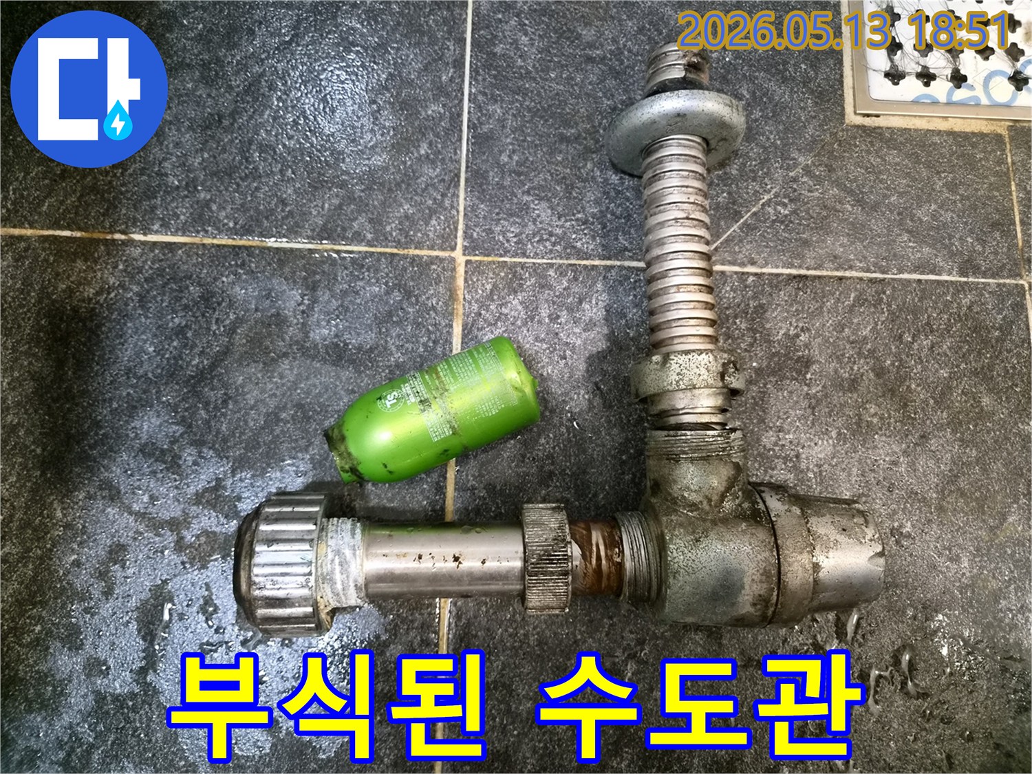 어두운 타일 바닥 위에-녹슨 수도관 부품과-초록색 용기가 놓여있는-누수 현장 증거 사진