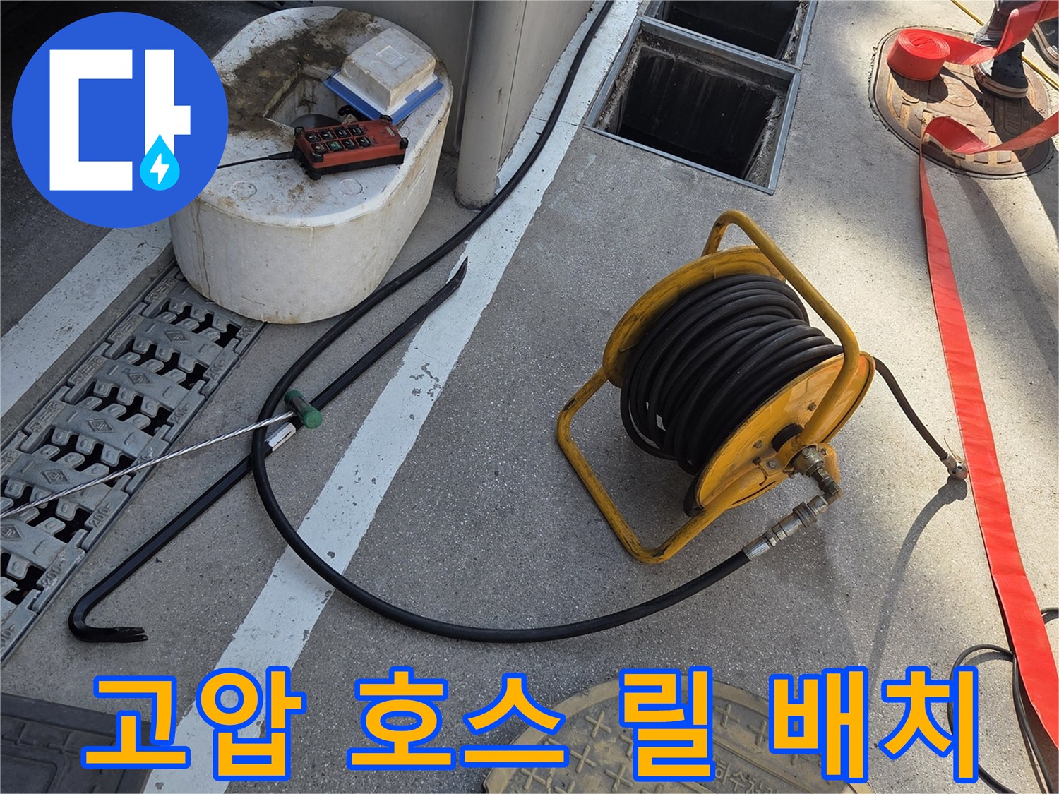 맨홀 옆에 놓인 노란색 고압 세척용 호스 릴과 호스