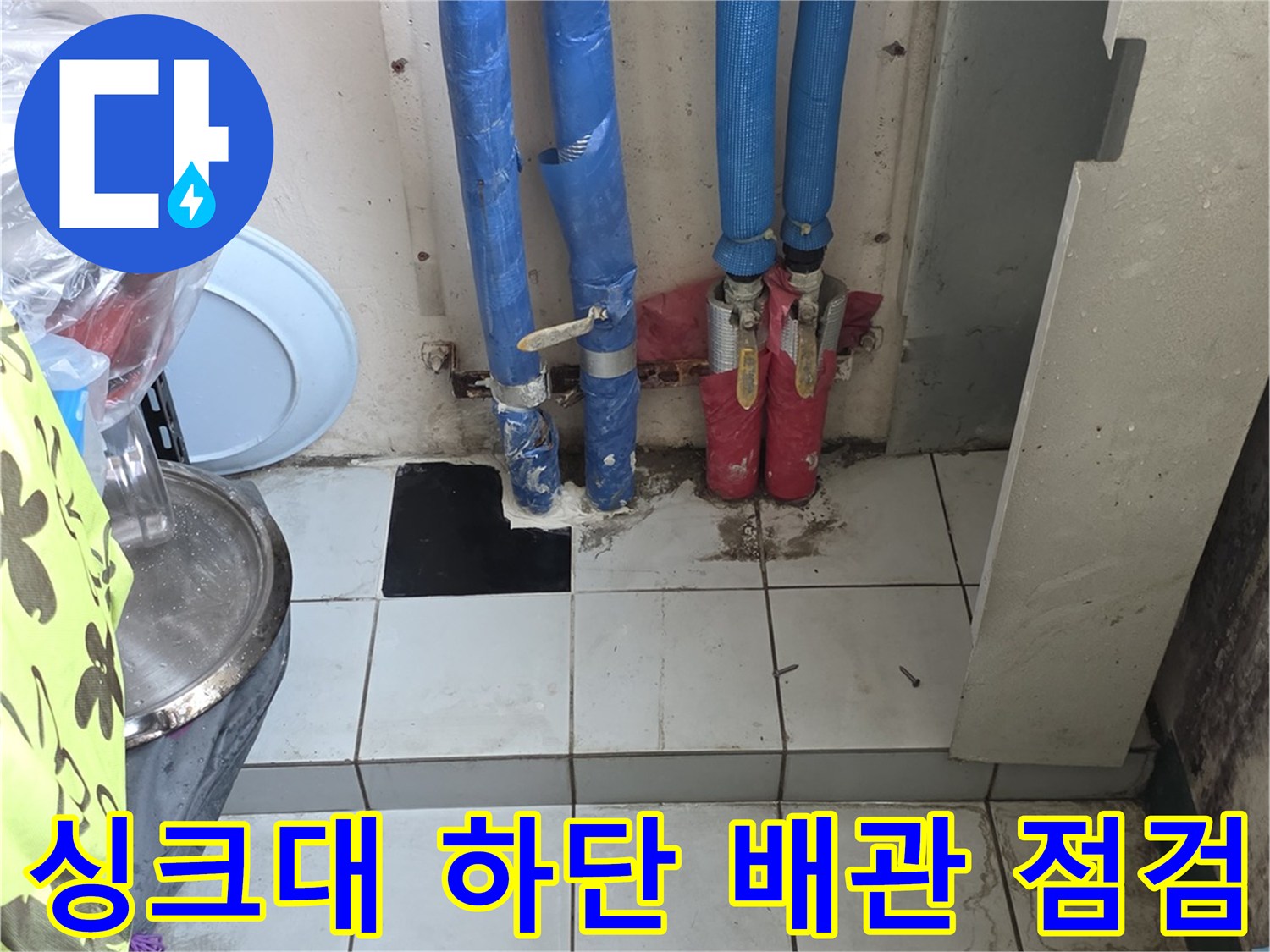 파란색 보온재로 덮인 여러 개의 배관이 있는 싱크대 하부 모습
