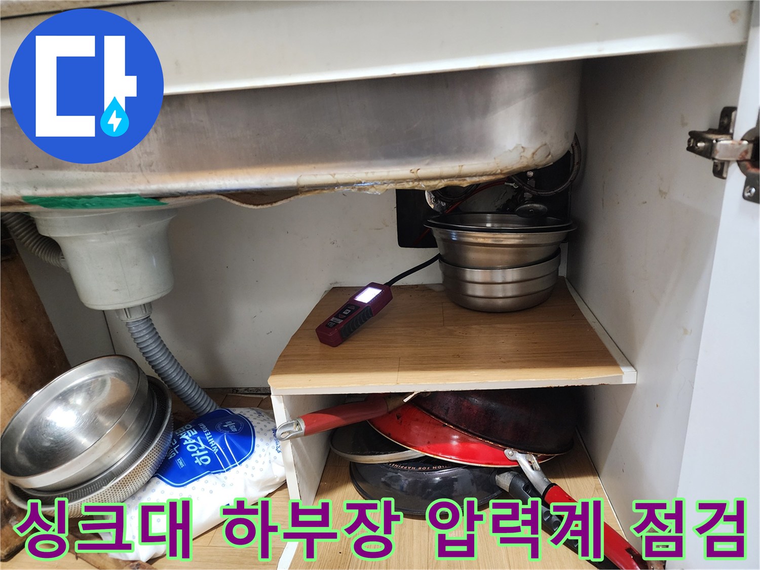 싱크대 하부장 선반 위에 놓인 디지털 압력 게이지와 배관 상태 확인 사진