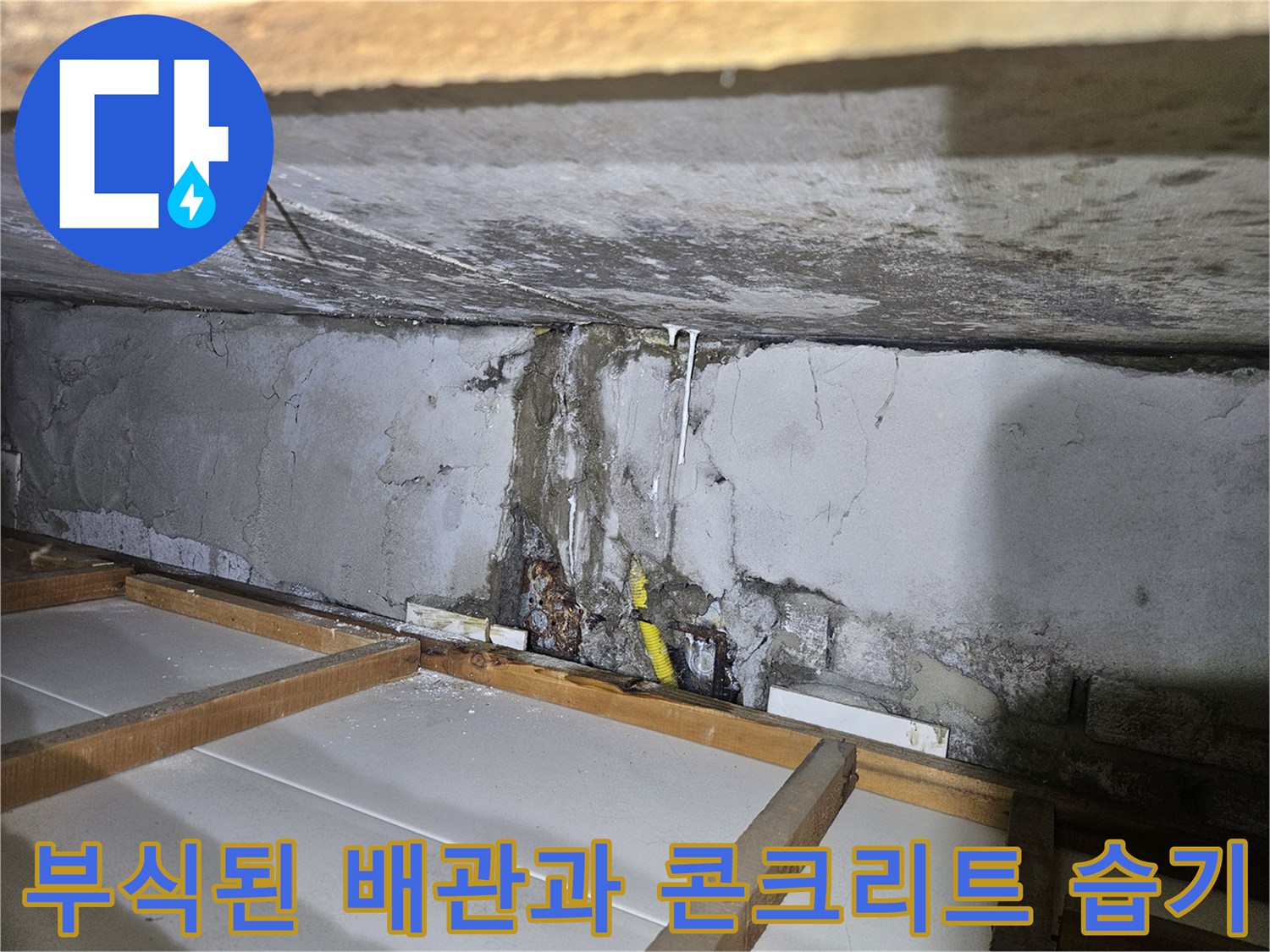 콘크리트 벽면 사이로 보이는 부식된 노란색 배관과 물자국