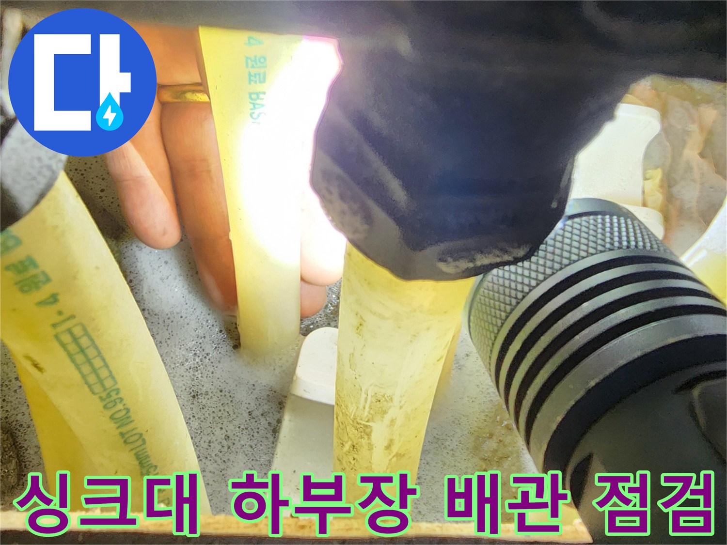 손전등으로 싱크대 아래 분배기 배관 연결부를 세밀하게 확인하는 모습