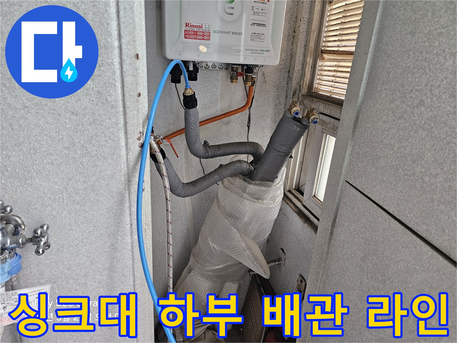 보온재가 씌워진 배관과 파란색 호스가 보이는 싱크대 내부